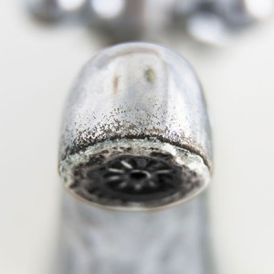 Hard water scale on the mouth of a silver faucet