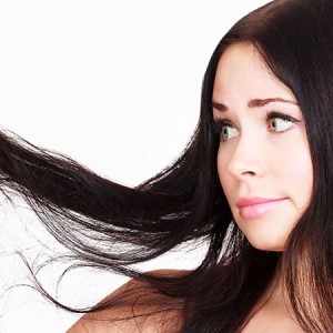 A woman holding out her brunette hair and looking at it with a disappointed facial expression