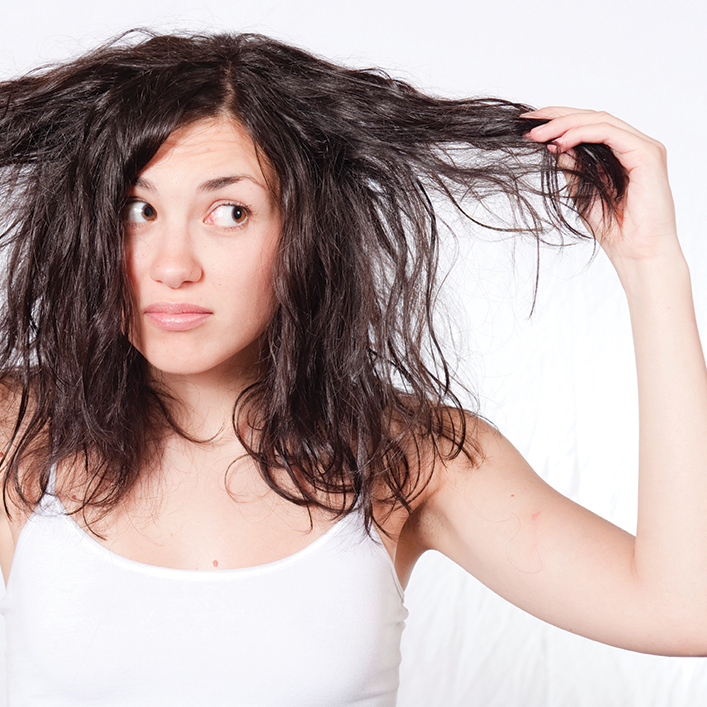 Woman holding out her hair and looking at it with a concerned expression