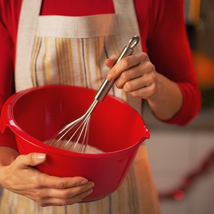 A person mixing baking ingredients in a red bowl