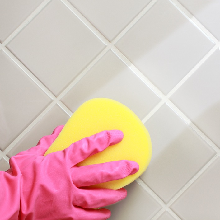A person’s gloved hand cleaning the bathroom tiles because of hard water stains