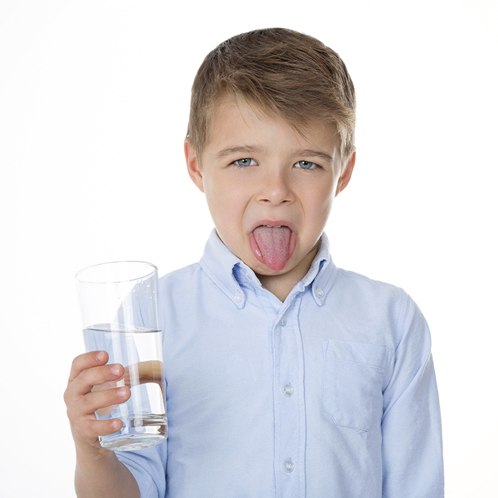 Kid sticking his tongue out in disgust while holding a glass of water