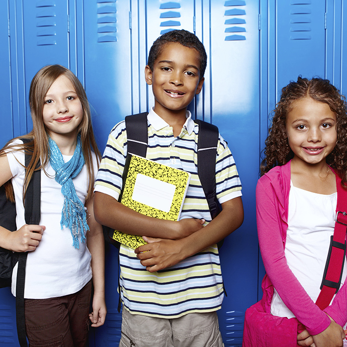Three kids standing next to each other smiling at the camera in front of blue lockers
